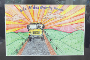 Bentley's poster - the front of a school bus, driving down a country road with fields of green on either side and a yellow and red sunset behind the bus.