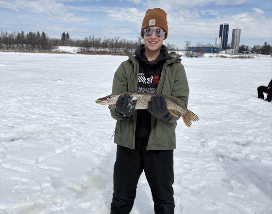 Person holding a large fish, standing on snow with a winter landscape.