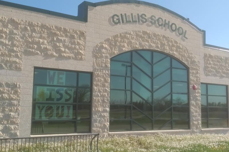A picture of the front of Gillis School. It shows 3 large windows a Tyndall stone exterior with the name of Gillis School on the front of the building