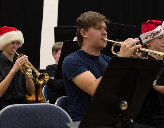 Musicians playing trumpets in a band, wearing festive Santa hats during a performance.