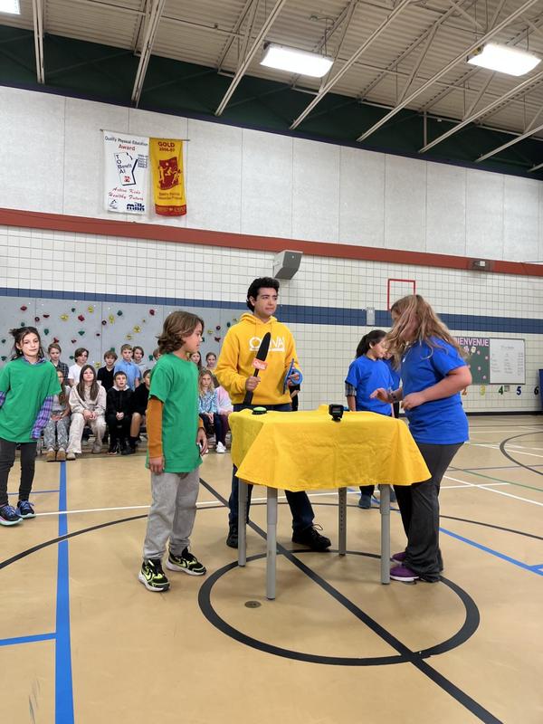 Student in green and student in blue facing off during the game show with the host in the background