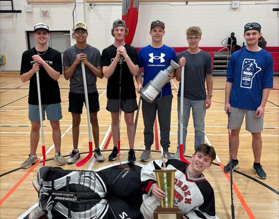 A group of seven young men celebrating a sports victory, with a trophy in the front.