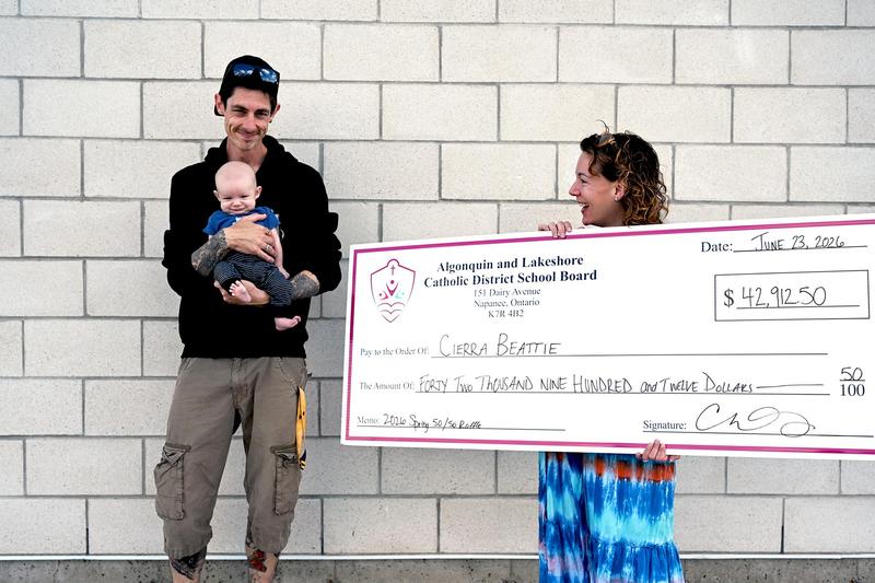 Raffle winner holding the large cheque with her partner and three month old baby.