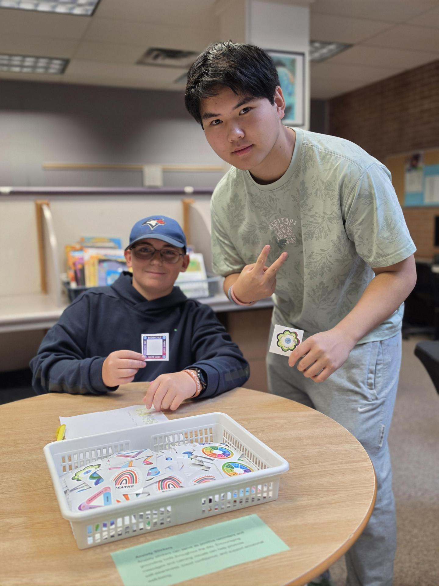 two students at a table with one giving the peace sign
