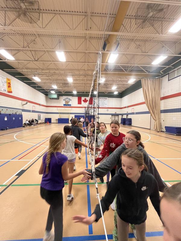 Two teams of students high fiving and saying good game on either side of a volleyball net.