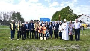 A large group of people standing together, smiling in hard hats and two students in the front holding shovels.