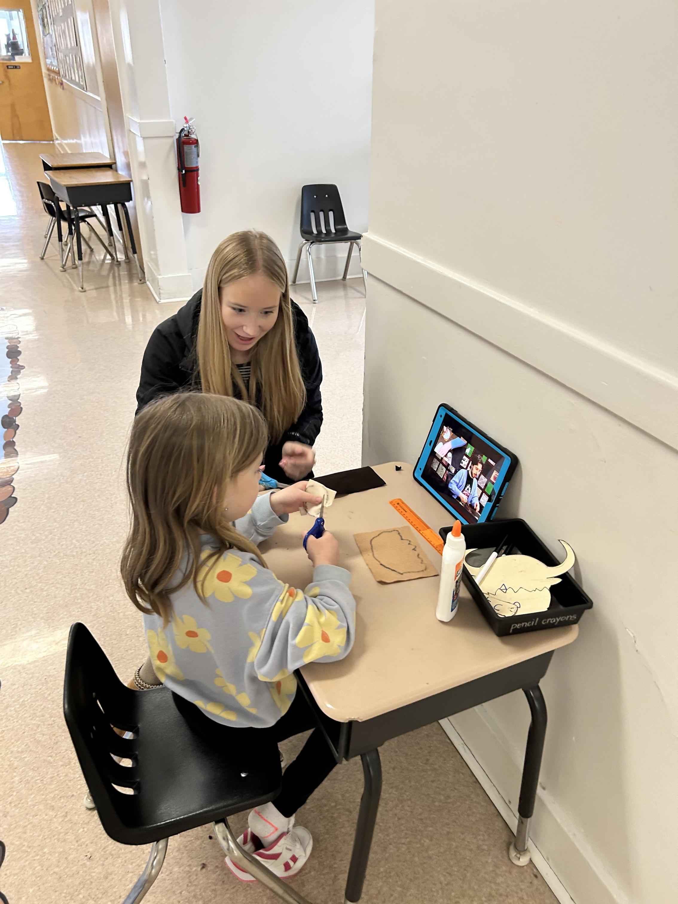 A high school student sits and works with an elementary student.