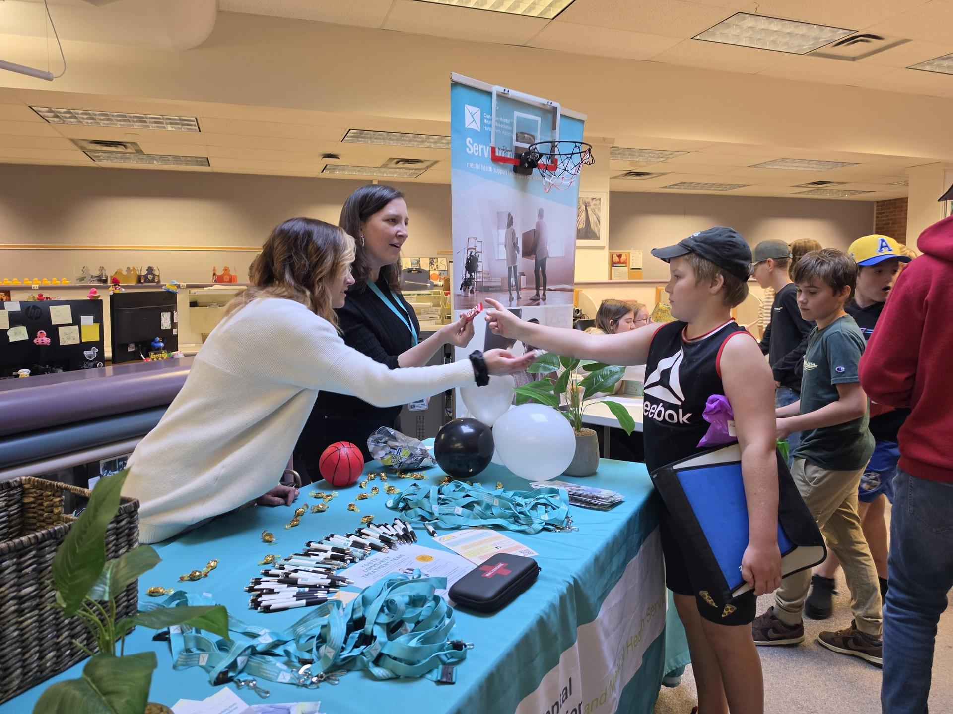 A student speaks to two women who are near a table and display about mental health services