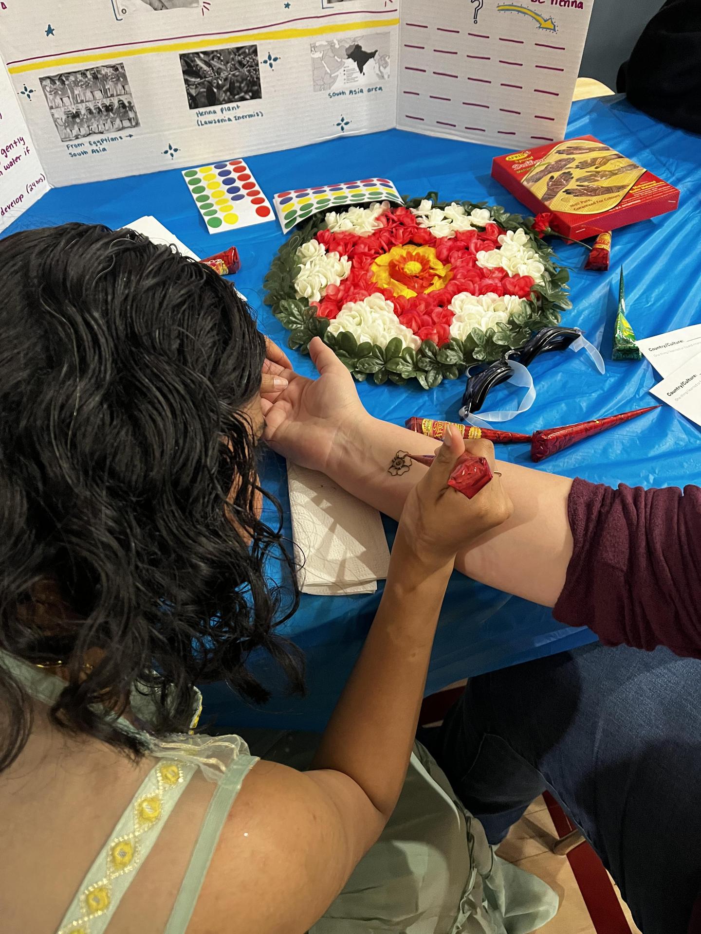 Student drawing henna on another student's wrist