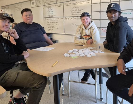 Five students gathered around a table, engaged in a group activity in a classroom.