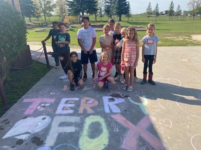 Group of students standing outside in front of a chalk picture they drew