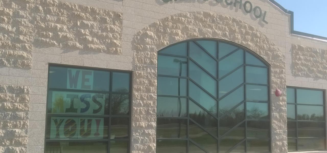 A picture of the front of Gillis School. It has 3 large windows, a Tyndall stone exterior finish and shows Gillis School at the top front of the building.