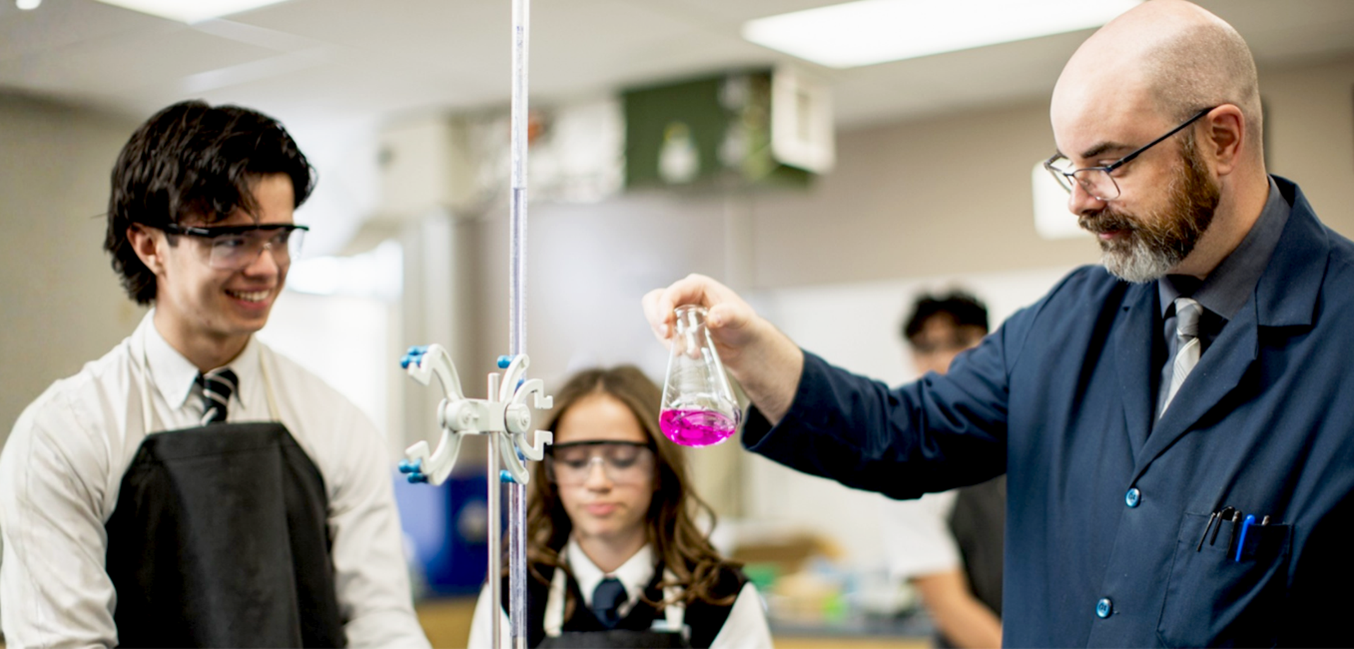 A teacher demonstrates an experiment with a magenta liquid while students observe attentively.
