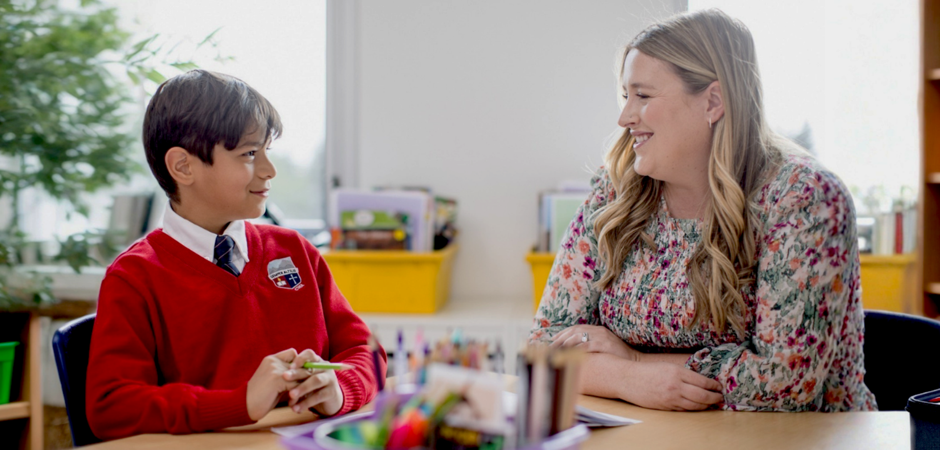 A smiling boy in a red sweater engages in conversation with a woman in a floral blouse.