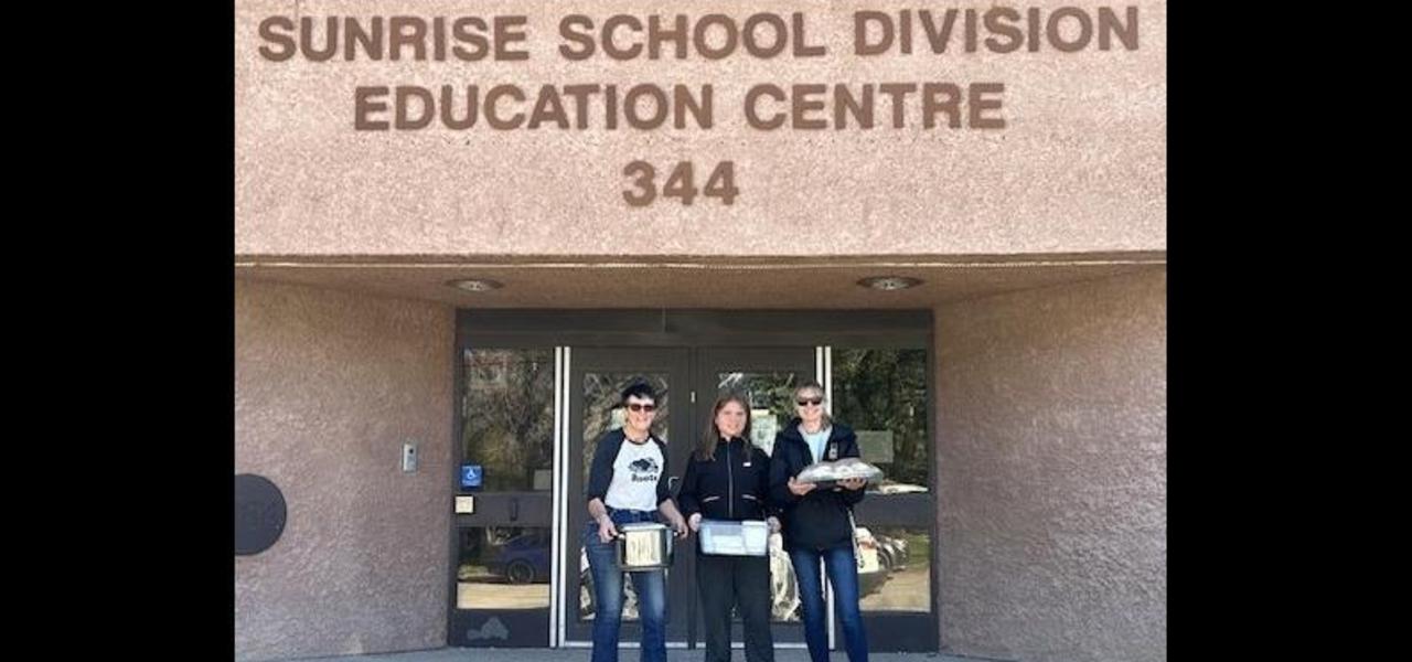 One student, one EA and one business owner holding food dishes standing in front of Sunrise School Division Education Centre Building. The student is doing work experience.