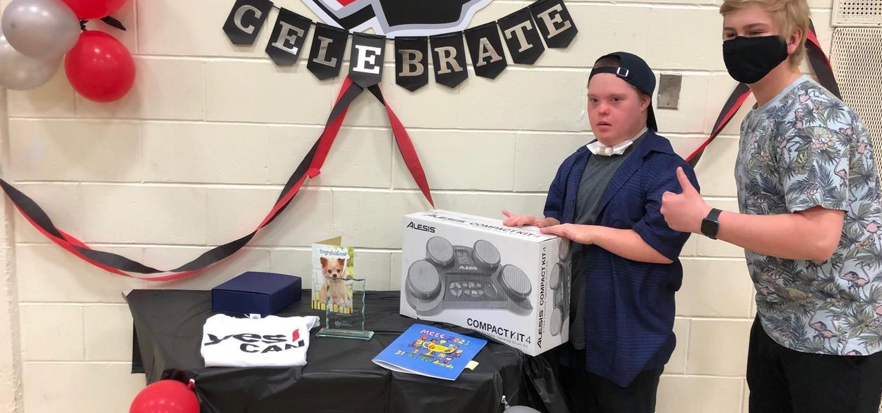 A student, accepting an award, standing beside a table that is decorated with balloons and a sign that says celebrate behind the table on the wall.