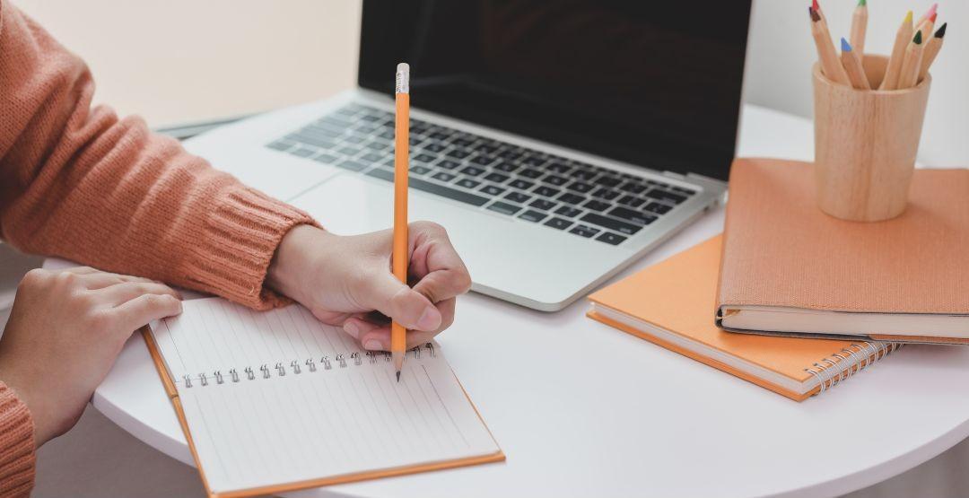 student working at a desk with note book and computer