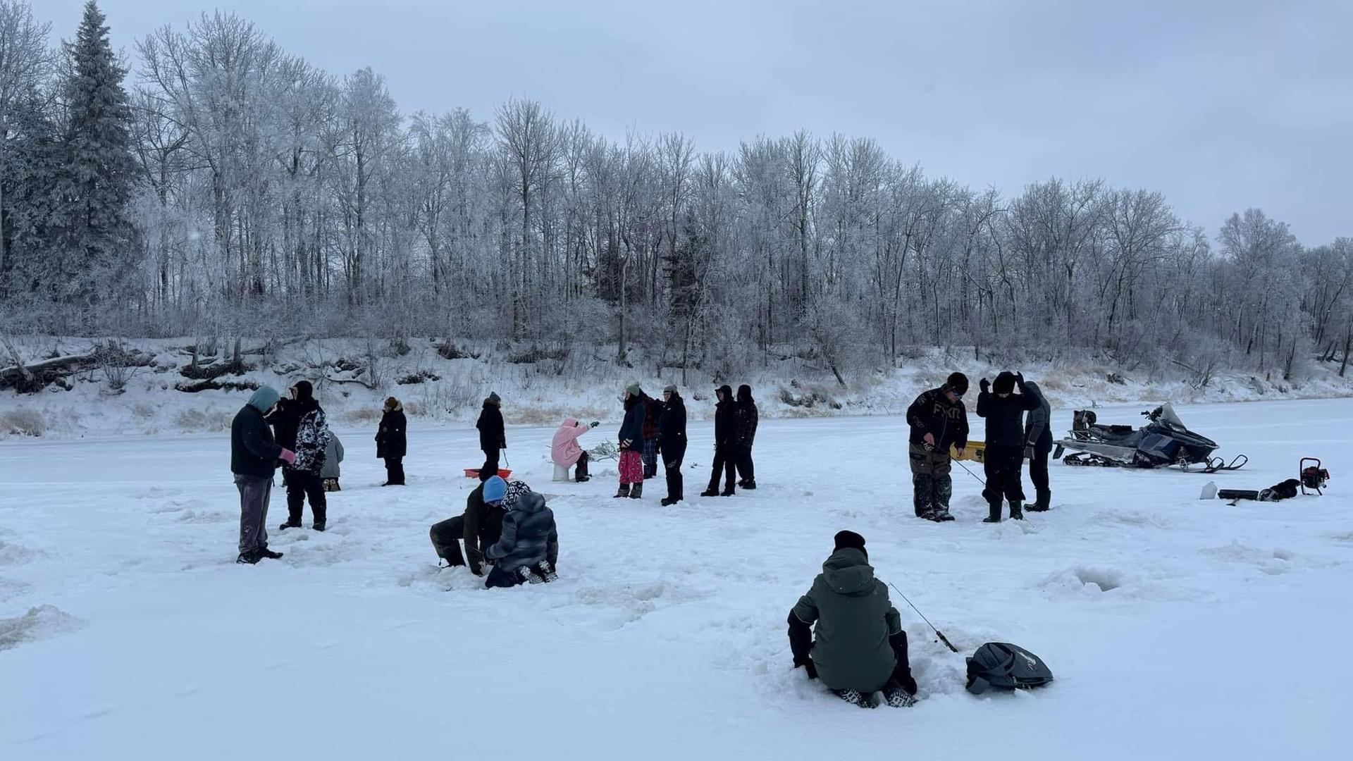 A crowd of people on a snowy landscape, some ice fishing, surrounded by frosted trees.