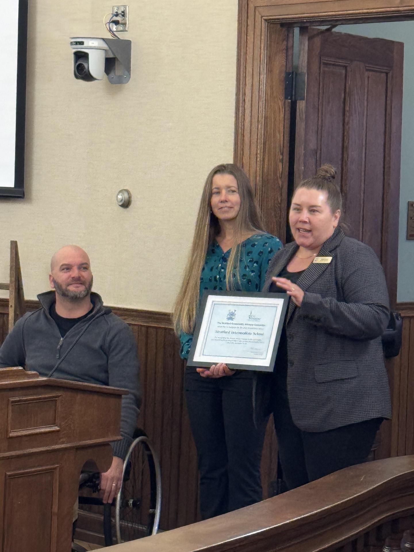 Cheri Carter holds the award while principal Erin Cassone and Roger Koert look on