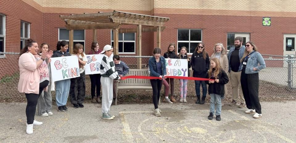 Group of students outside Anne Hathaway PS cutting a ribbon to introduce their "buddy bench"