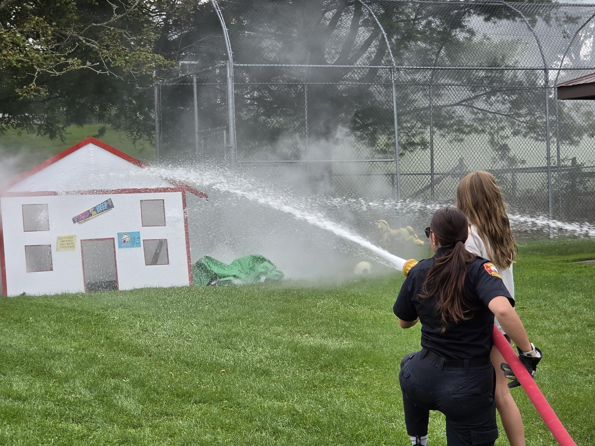 Young girl holding a fire hose pointed at a cardboard house