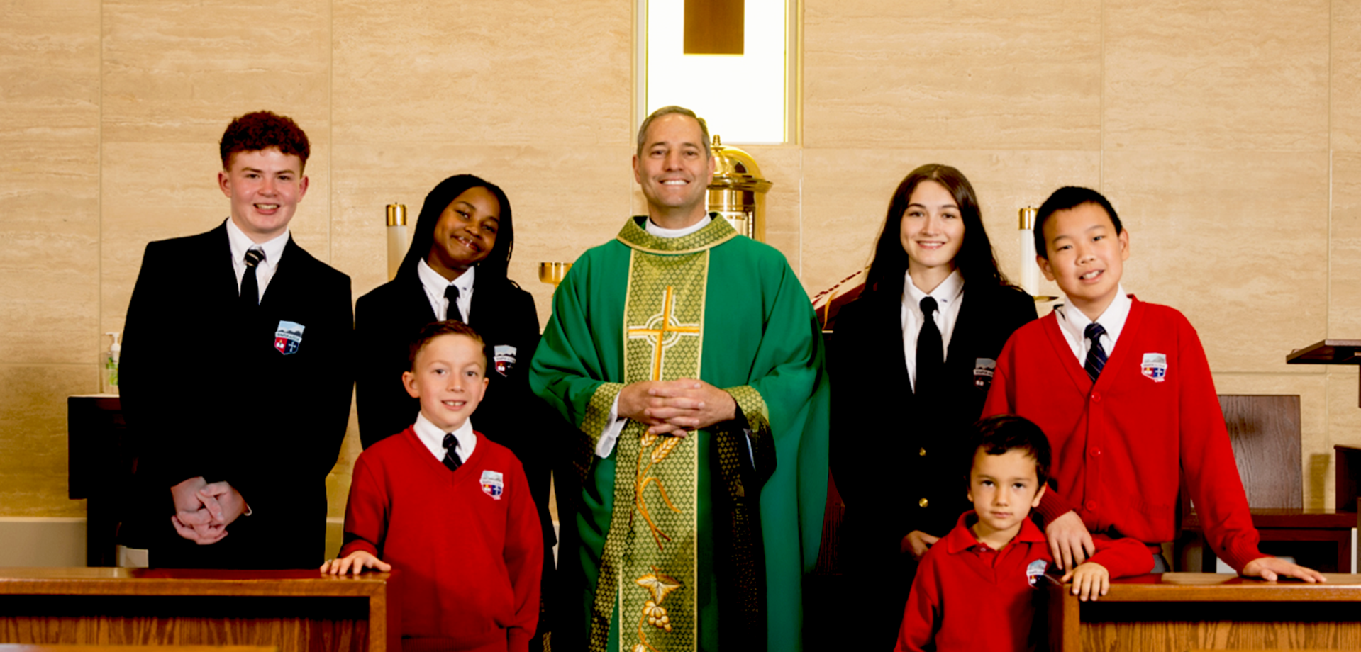 Six children and a priest in green vestments pose together in a church setting.