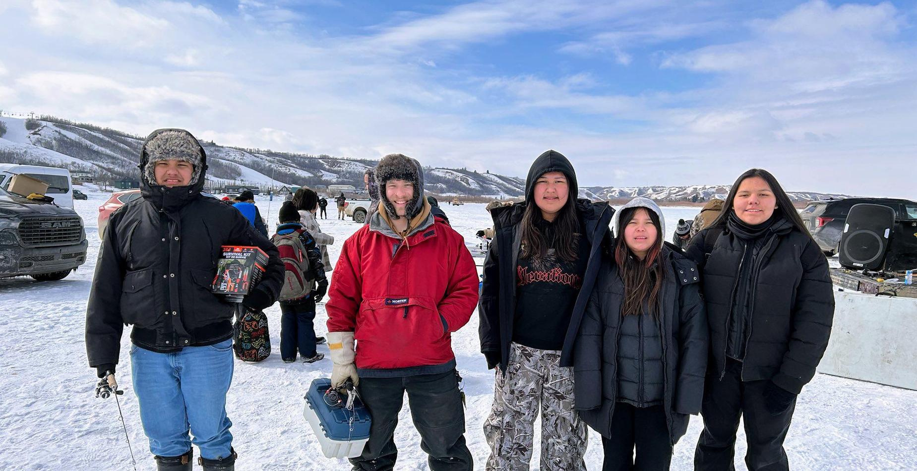 A group of five people in winter gear standing on a frozen lake for an ice fishing event.