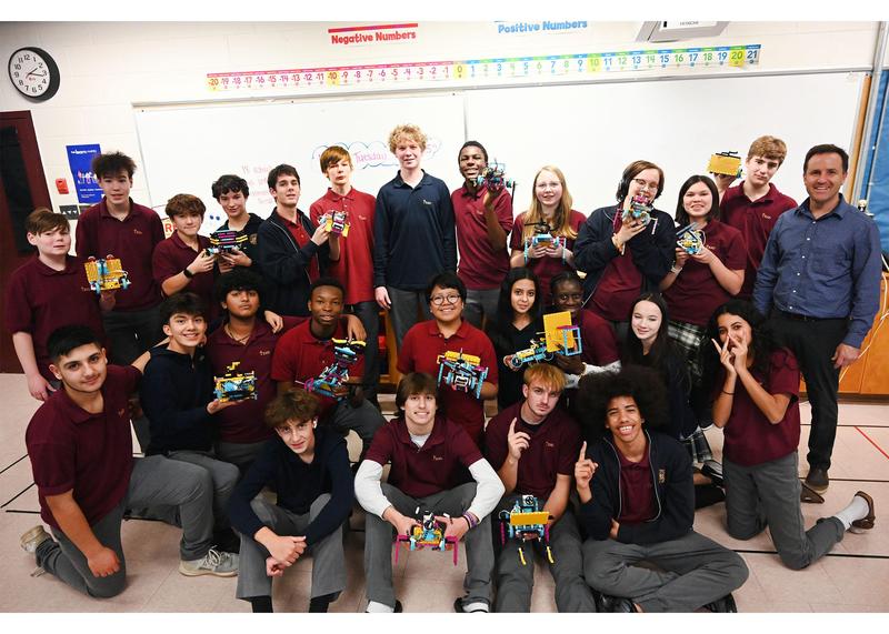 A large group of students holding up their Lego robotics and smiling for a posed picture