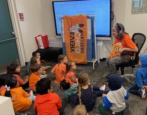 An adult teaches a group of children sitting on the floor in a classroom.
