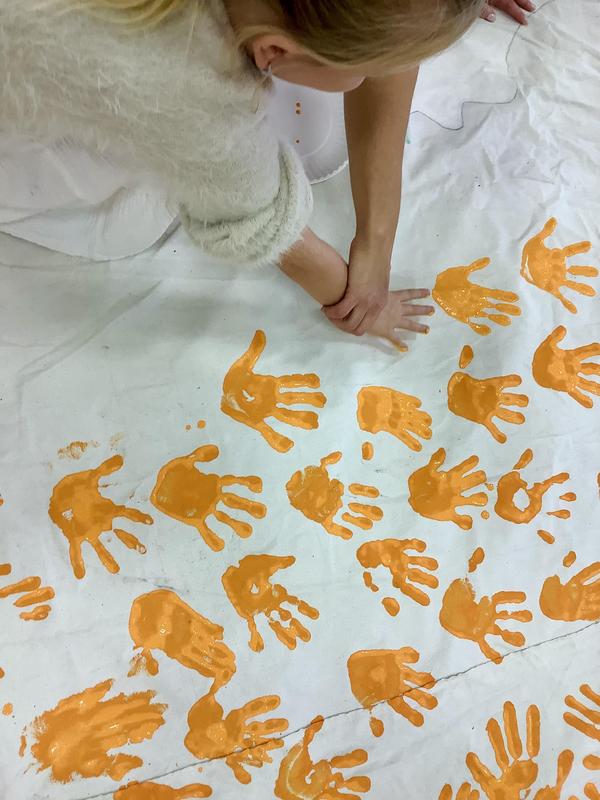 A student adds a painted orange handprint to the side of the tipi
