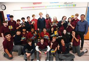 A large group of students holding up their Lego robotics and smiling for a posed picture