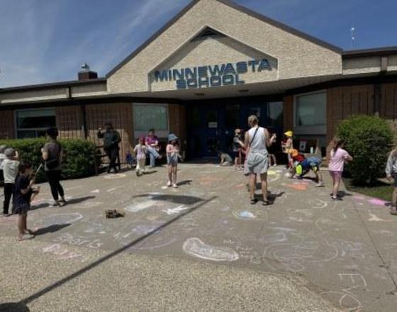 Children drawing with chalk on the sidewalk in front of Minnewasta School.
