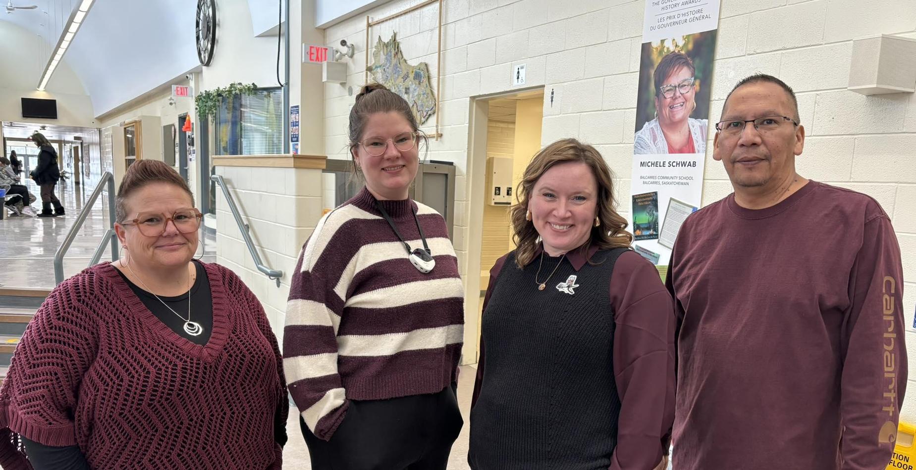 Four staff members standing together in a school hallway in front of a poster for the Governor General's History Awards.