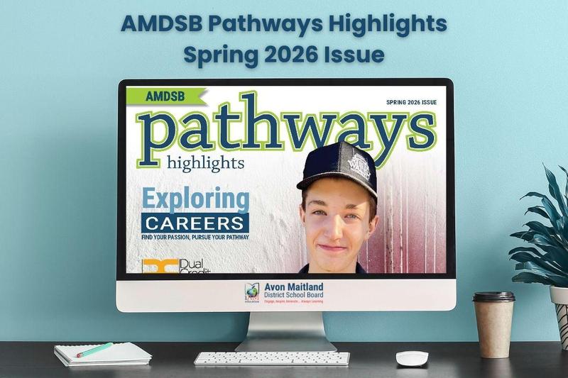 A computer monitor sitting on a desk displays the cover of the "AMDSB Pathways Highlights Spring 2026 Issue." The cover features a smiling high school student wearing a black cap, with the headline "Exploring Careers: Find your passion, pursue your pathway," and a "Dual Credit" logo in the corner. The computer sits in front of a light blue wall, which features the header text: "AMDSB Pathways Highlights Spring 2026 Issue."