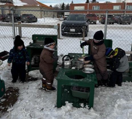 Children playing with toy kitchen equipment in a snowy outdoor area.