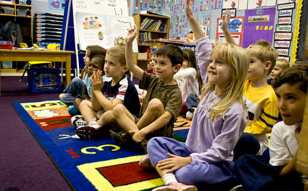 Kindergarten students sitting on a colourful carpet engaging with their teacher.