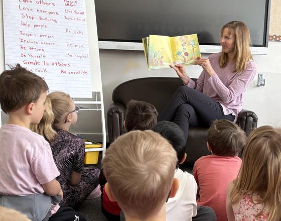 A teacher reading a story to a group of attentive children seated on the floor.
