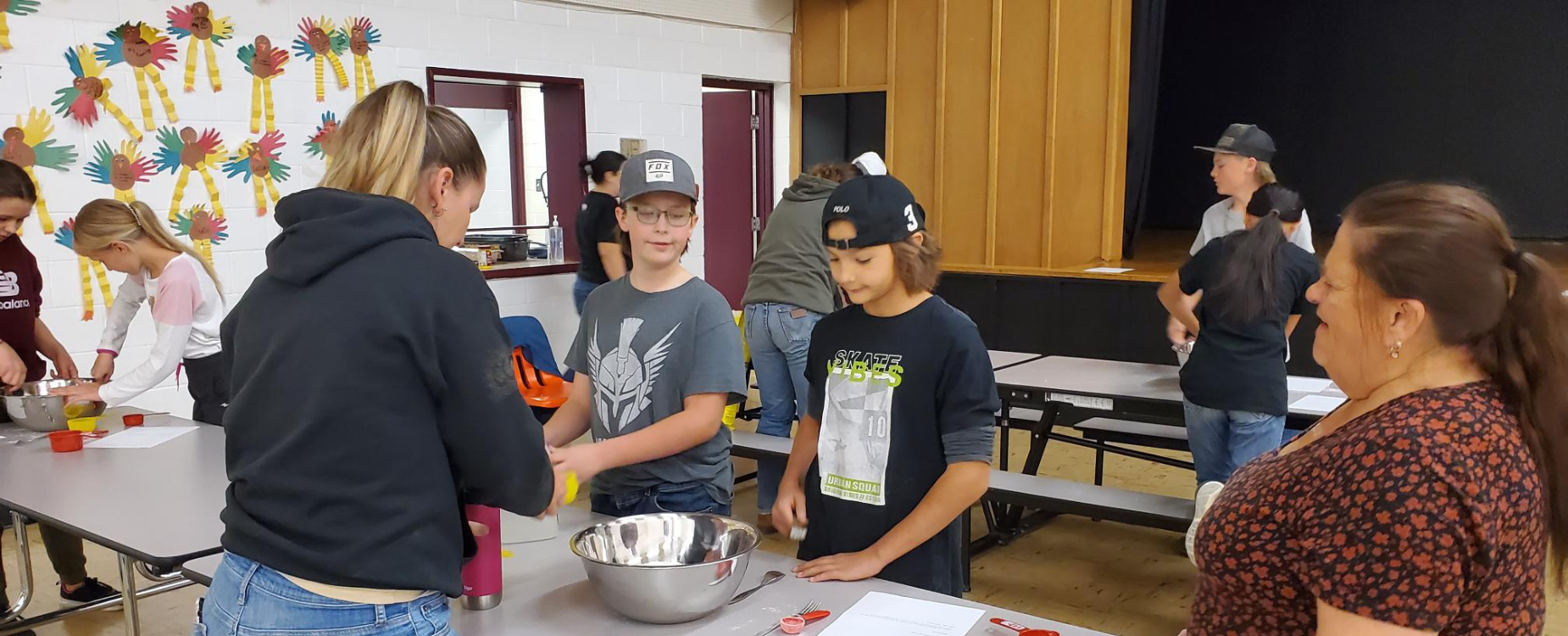 Middle school and high school students stand around tables measuring and adding baking ingredients into bowls.