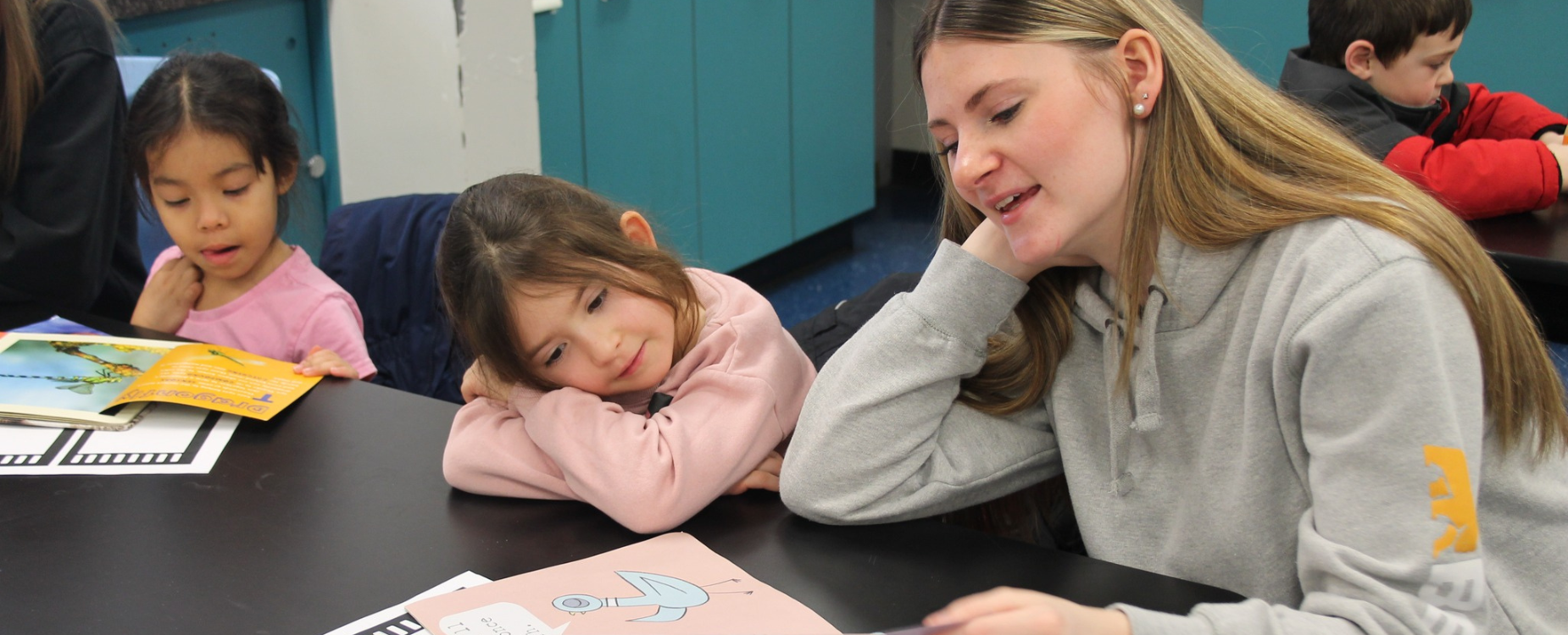 A highschool student reads to a young elementary student at a table.