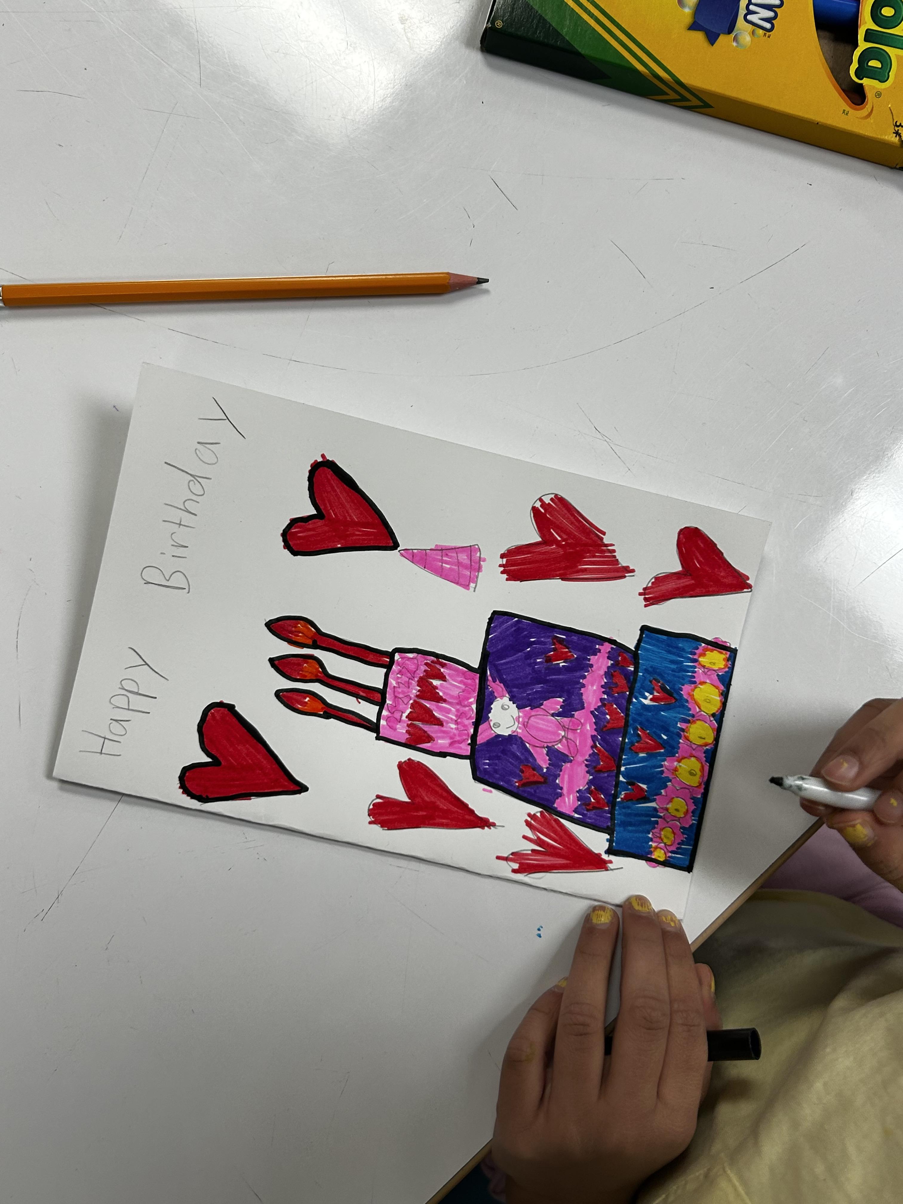 A birthday card drawn by a student featuring a layered cake and hearts on the cover.