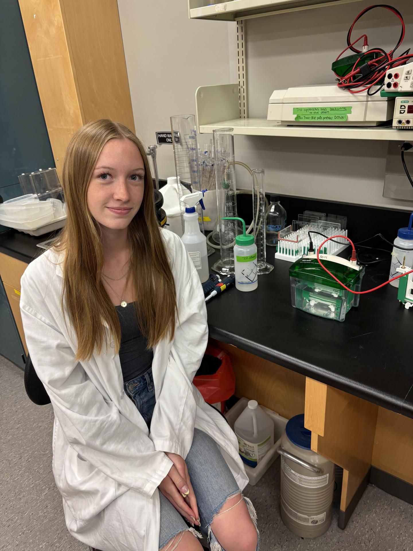 Female students sitting in lab beside her experiment
