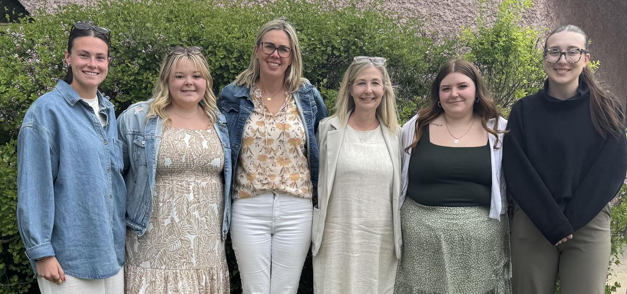 6 ladies standing in front of a bush smiling and posing for the camera.
