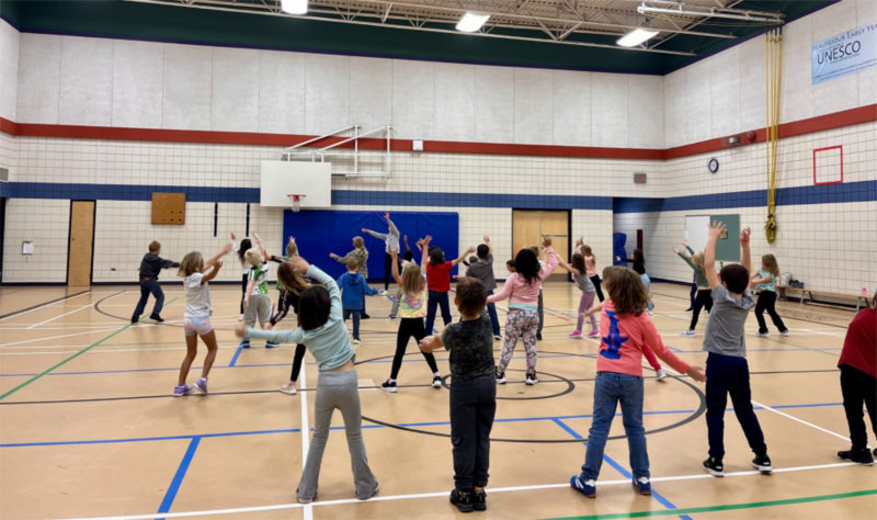 A group of students dancing, while being led by an instructor, in the gym