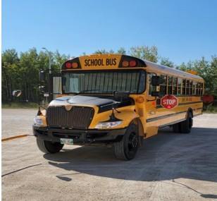 A picture of a school bus stopped in a parking lot with trees showing in the background.