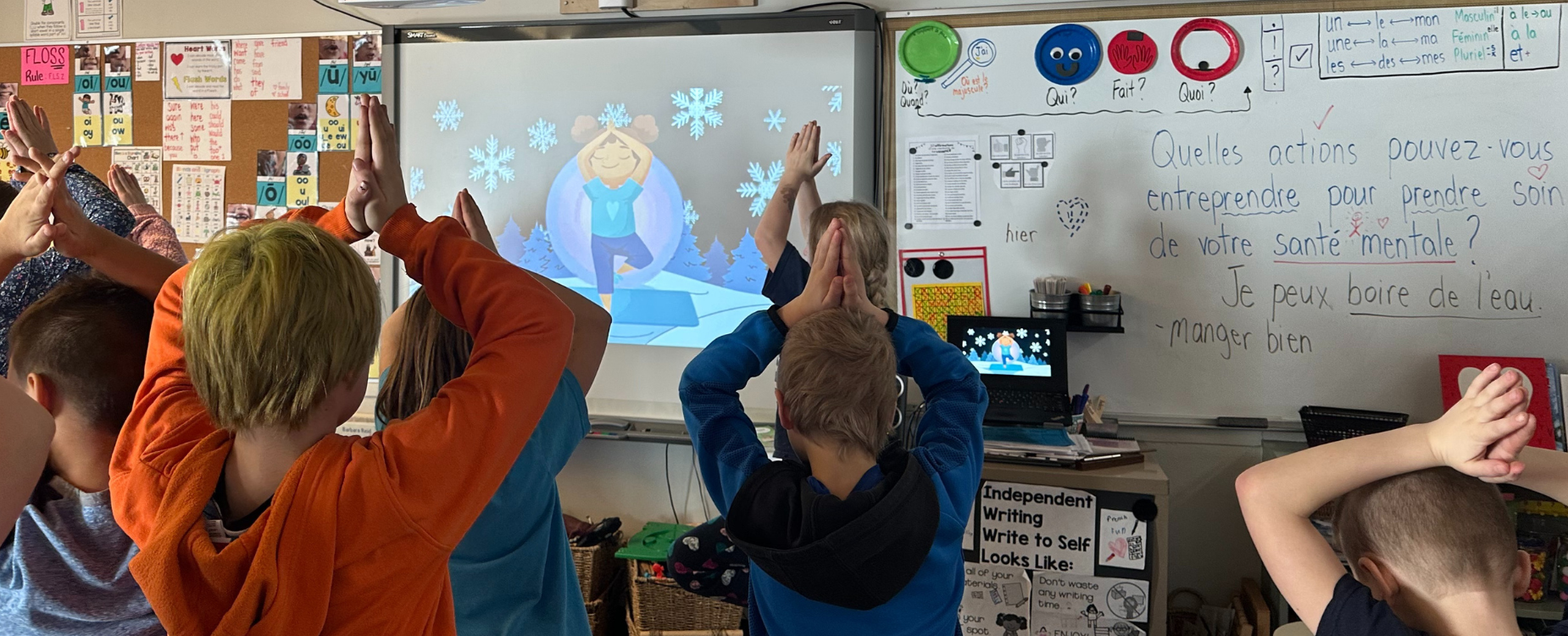 Elementary students in a classroom following along a cartoon video, doing a yoga tree pose.