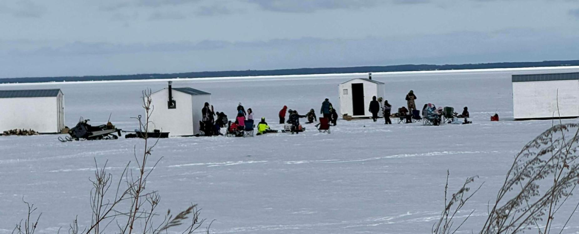 Students ice fishing outside. Also pictured is 4 ice fishing shacks.
