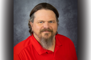Studio portrait of John Taylor wearing a red golf shirt, smiling at the camera.