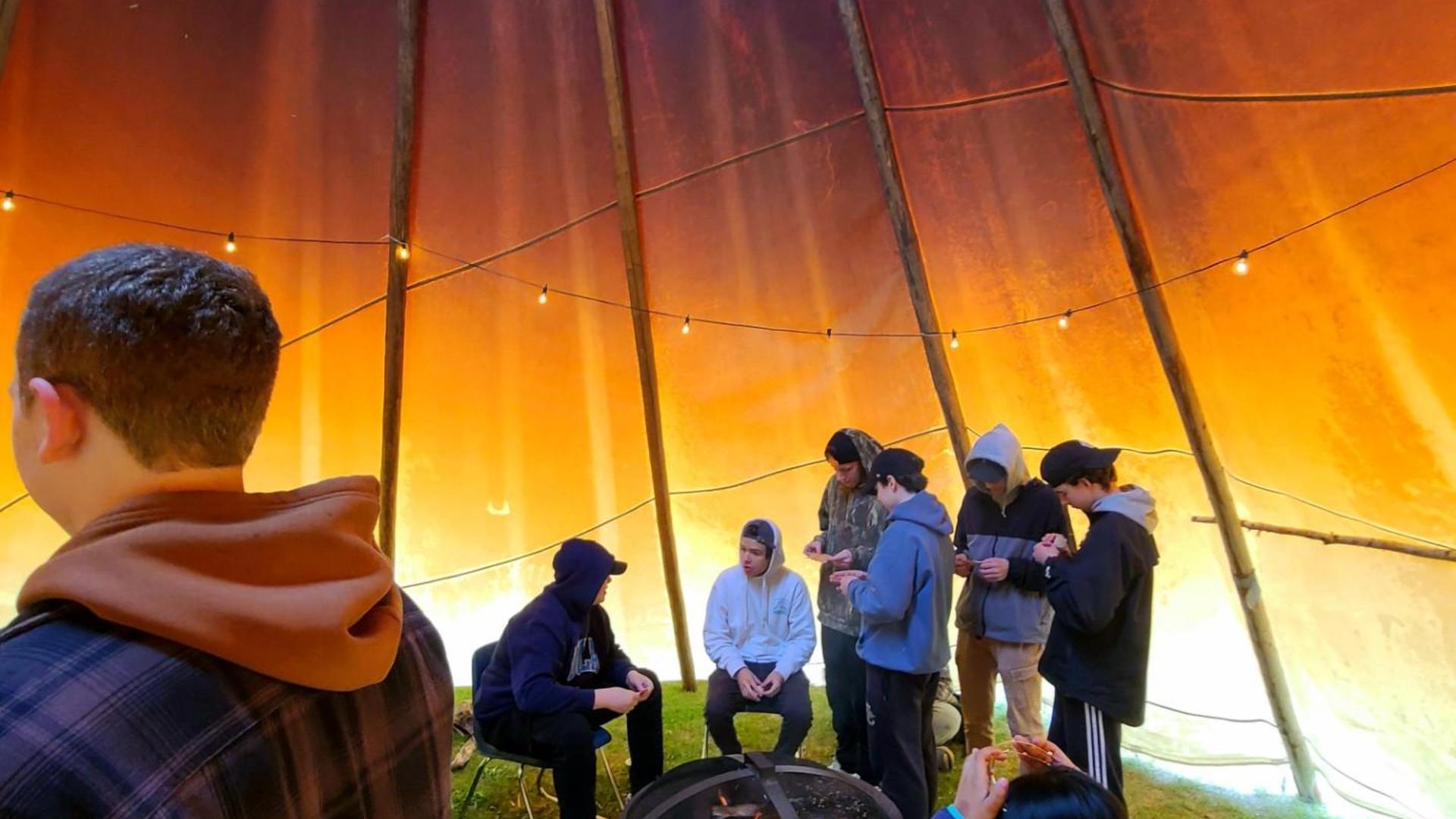 Group of people inside a tent around a central fire pit.