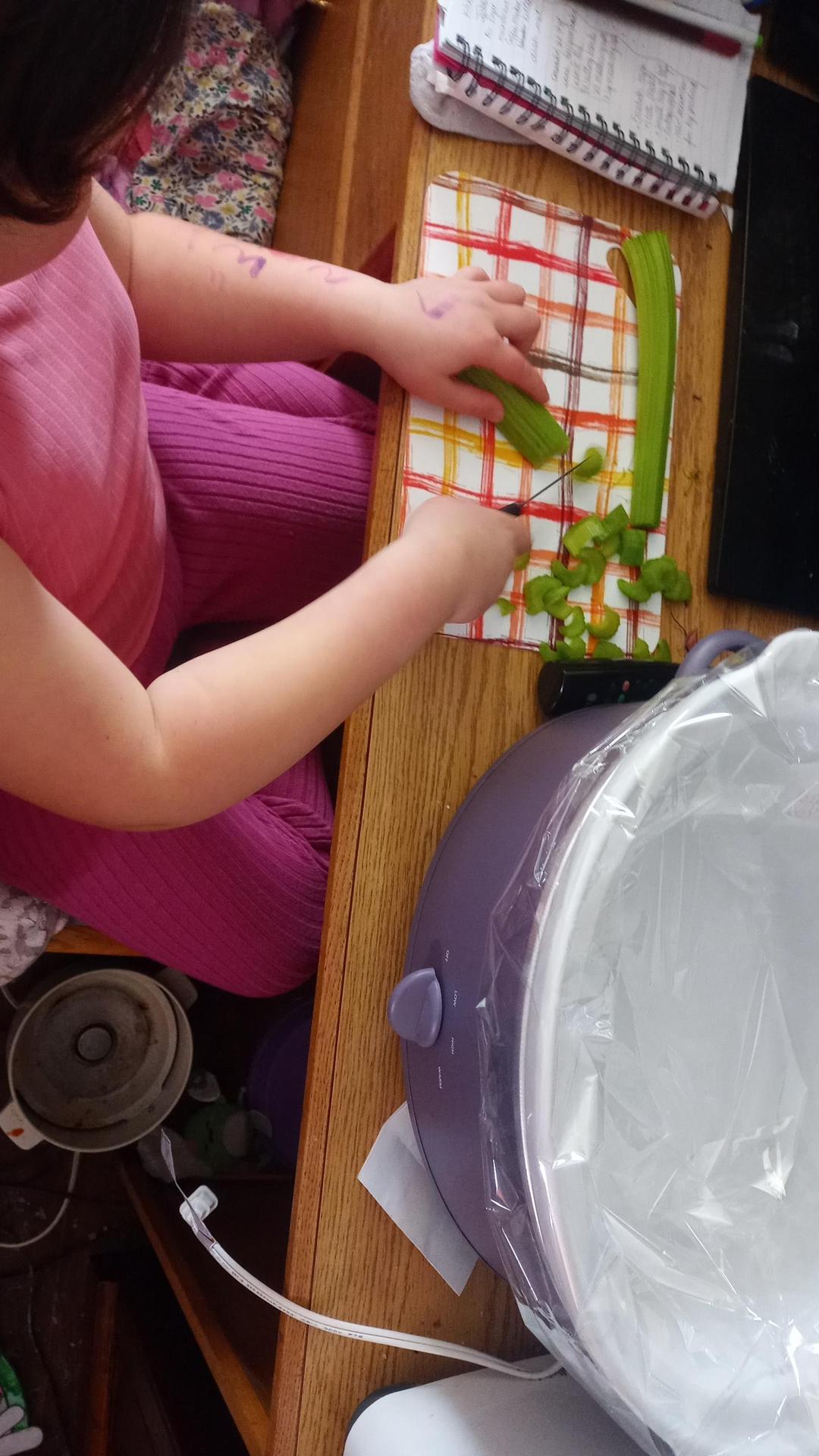 Student cutting vegetables beside a crock pot