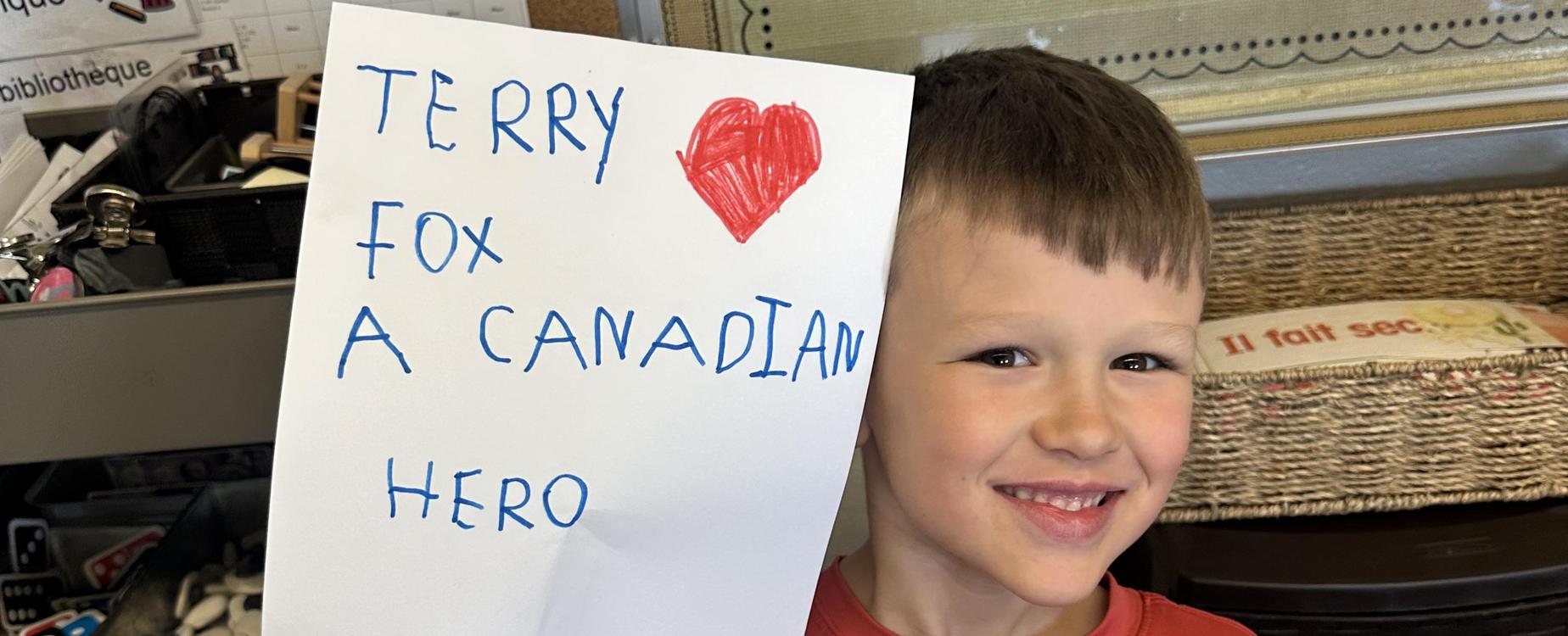 Student with a terry fox poster he made that says Terry Fox a Canadian Hero.